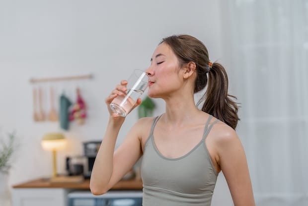 a woman drinking water from a clear glass