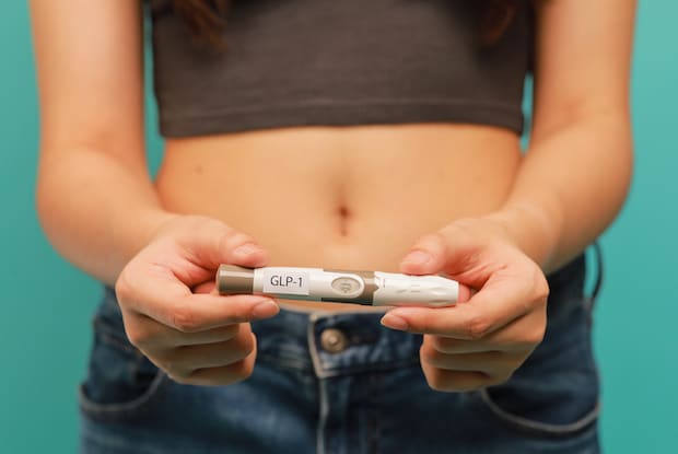 a woman holding up a GLP-1 injection pen