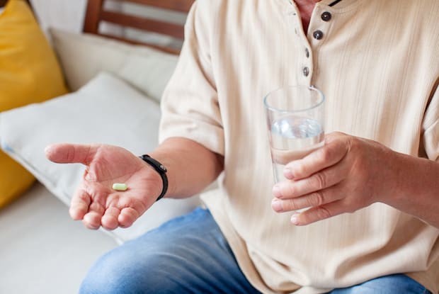a man holding a pill in one hand and a cup of water in the other hand
