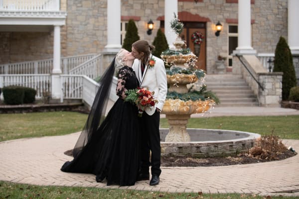 Bride and groom kissing by a fountain, bride in a black A-line gown and black veil