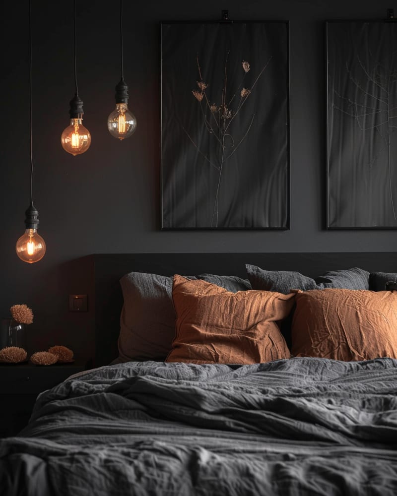 Modern dark bedroom featuring matte black walls, Edison bulb pendants, wrinkled linen bedding, terracotta pillows, botanical artwork, and moody minimalist design