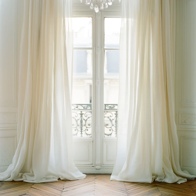 Parisian apartment featuring floor to ceiling white silk curtains crystal chandelier herringbone floors and ornate iron balcony