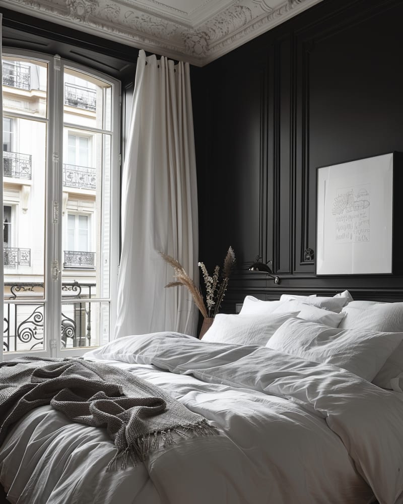Parisian dark bedroom featuring ornate crown molding, matte black walls, white linen bedding, French windows, grey throw blanket, minimalist artwork, dried flowers, and monochromatic design