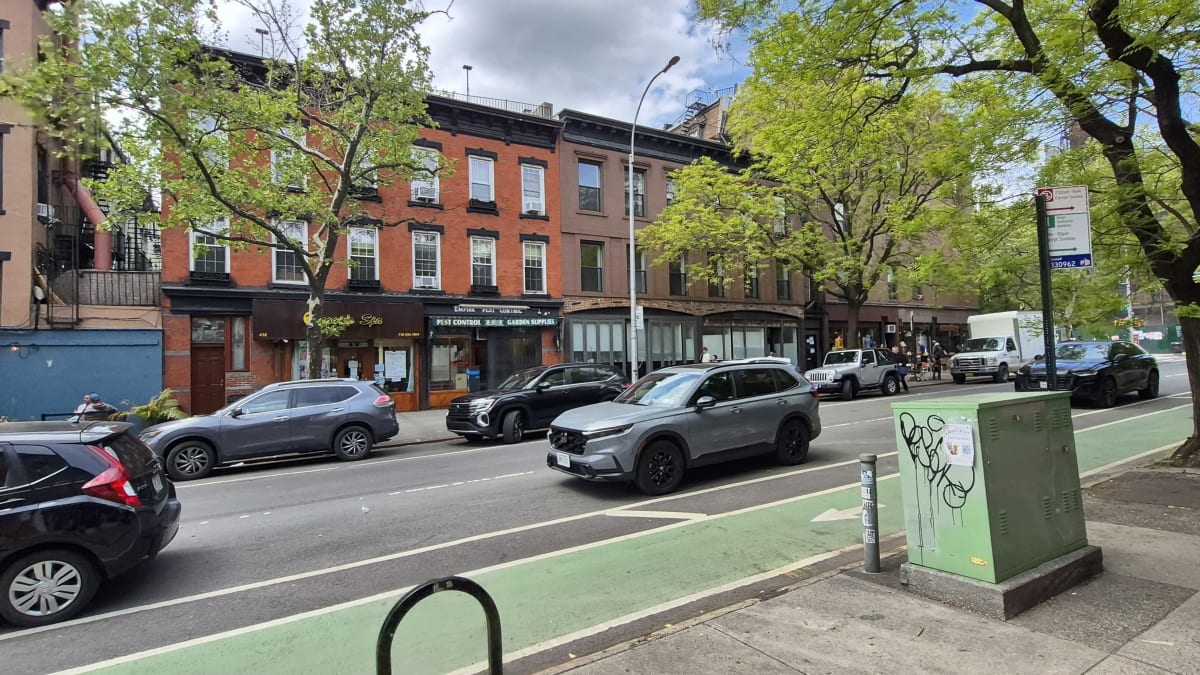 Low red-brick buildings with storefronts along a street with a green bike lane and passing cars