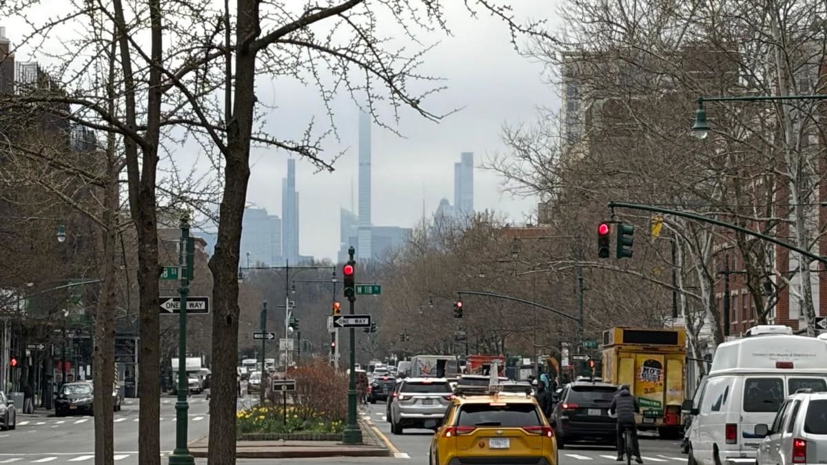 A wide tree-lined boulevard with traffic and the misty Midtown skyline of supertall towers beyond