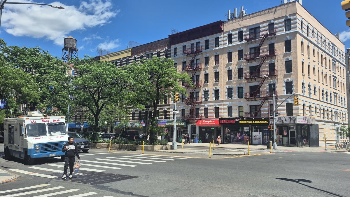 Six-story prewar apartment building with fire escapes and a rooftop water tank above corner shops