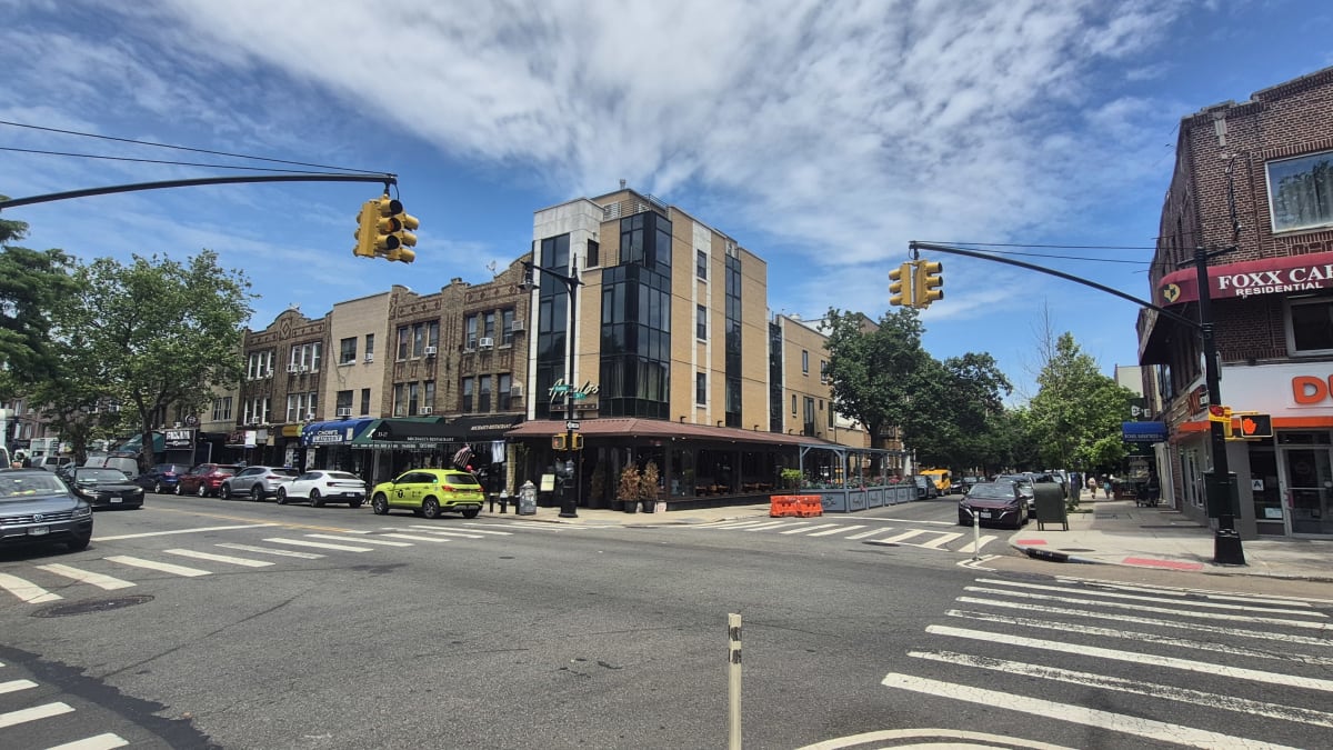 A wide commercial intersection lined with low brick buildings, storefronts, and crosswalks