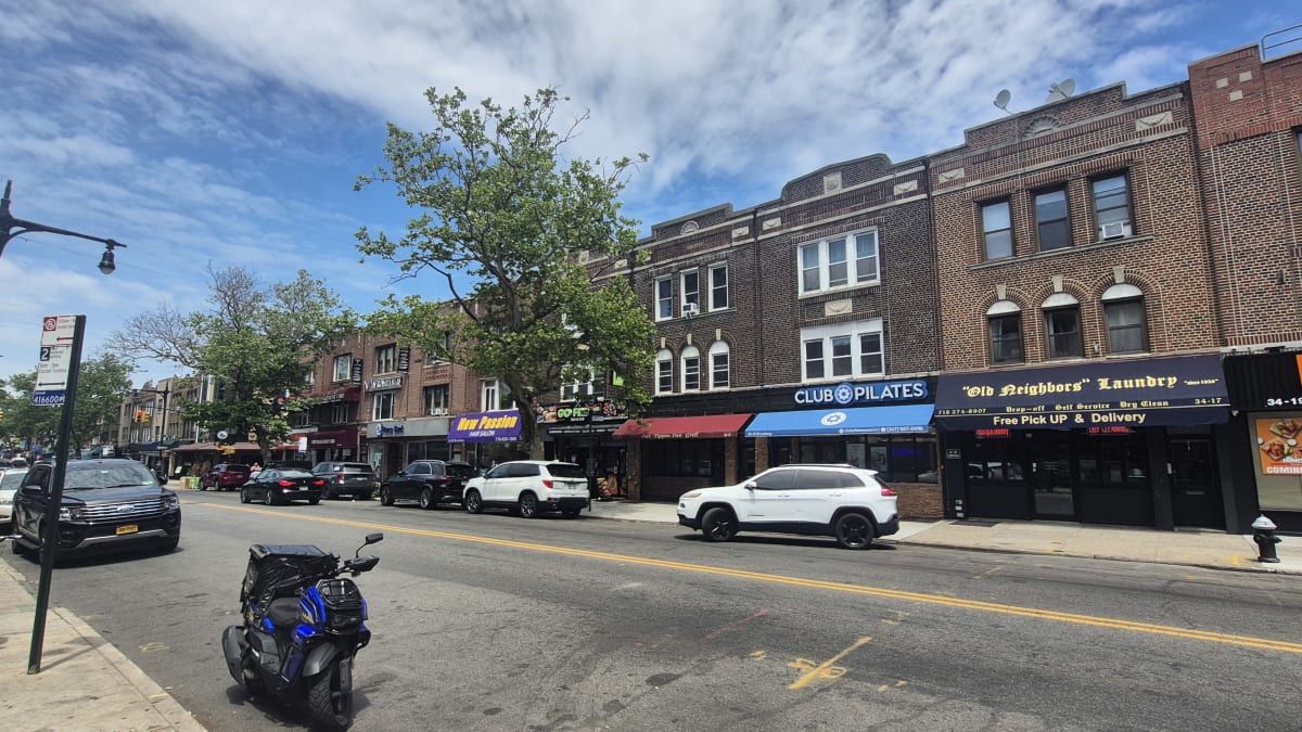 Low brick storefront buildings along a wide commercial street with parked cars and a scooter