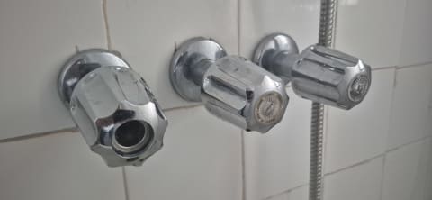 Close-up of chrome faucet handles and a shower fixture on a white tiled bathroom wall