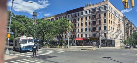 Six-story prewar apartment building with fire escapes and a rooftop water tank above corner shops
