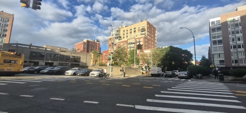 A wide multi-lane intersection with crosswalks, a city bus, and mid-rise brick apartment buildings beyond