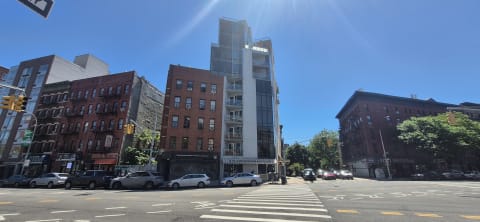 A new glass mid-rise apartment building beside older red-brick walk-ups at a street corner