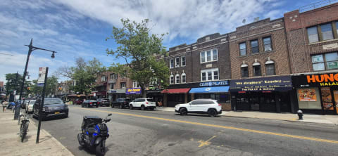 Low brick storefront buildings along a wide commercial street with parked cars and a scooter