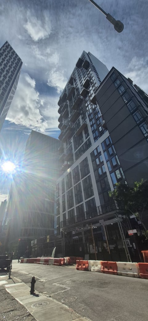 Tall modern residential towers rising above street-level construction barriers, with sun flaring against a blue sky