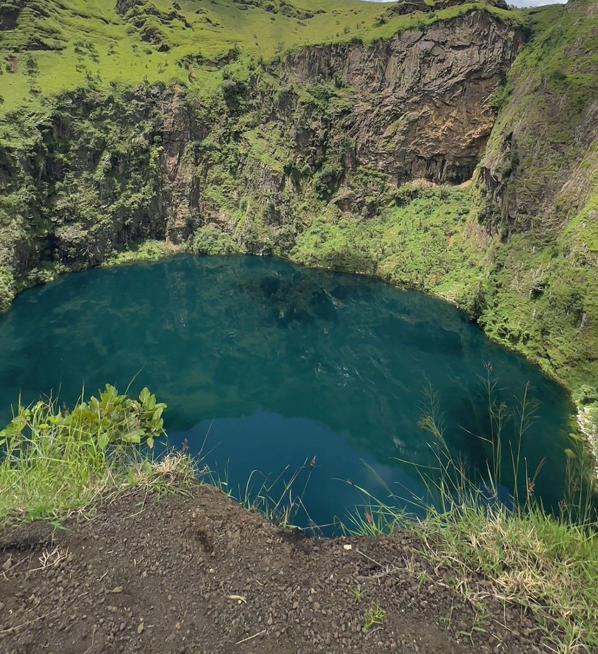 Mirror-like waters of a mystical jungle crater lake reflect the serene, untouched beauty of Cameroon.