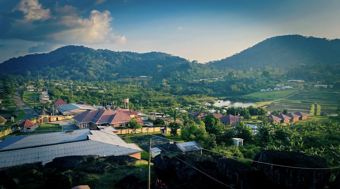 A stunning valley town cradled by emerald mountains under a golden tropical glow 