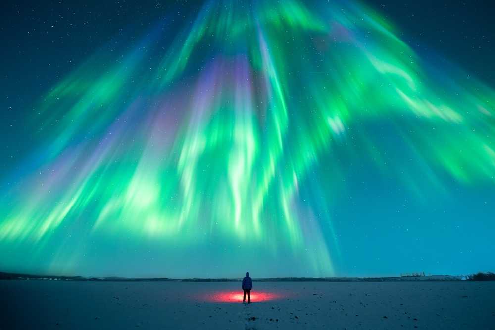 Northern lights glowing above a snowy Iceland landscape with a traveler below
