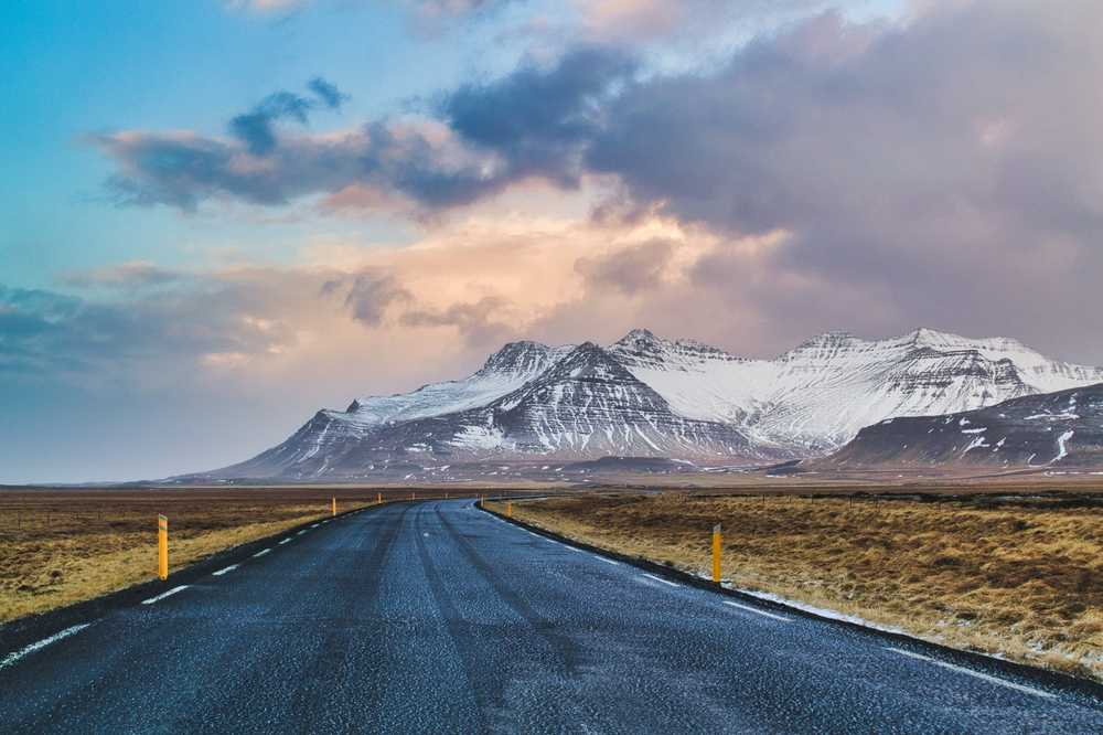 Open Iceland road leading toward snow-covered mountains under dramatic clouds
