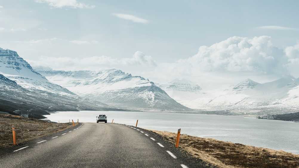 Car driving along an open Iceland road beside snowy mountains and a fjord