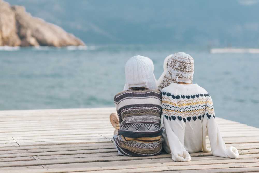 Two travelers in wool sweaters sitting by the water during a quiet Iceland trip