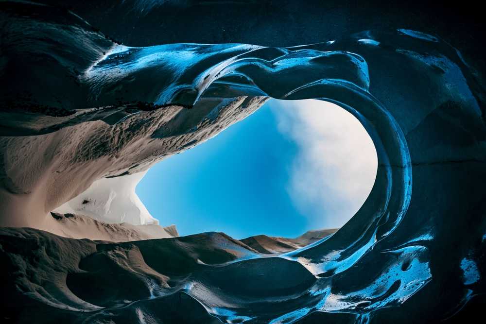 View from inside a blue ice cave looking out toward the Icelandic landscape