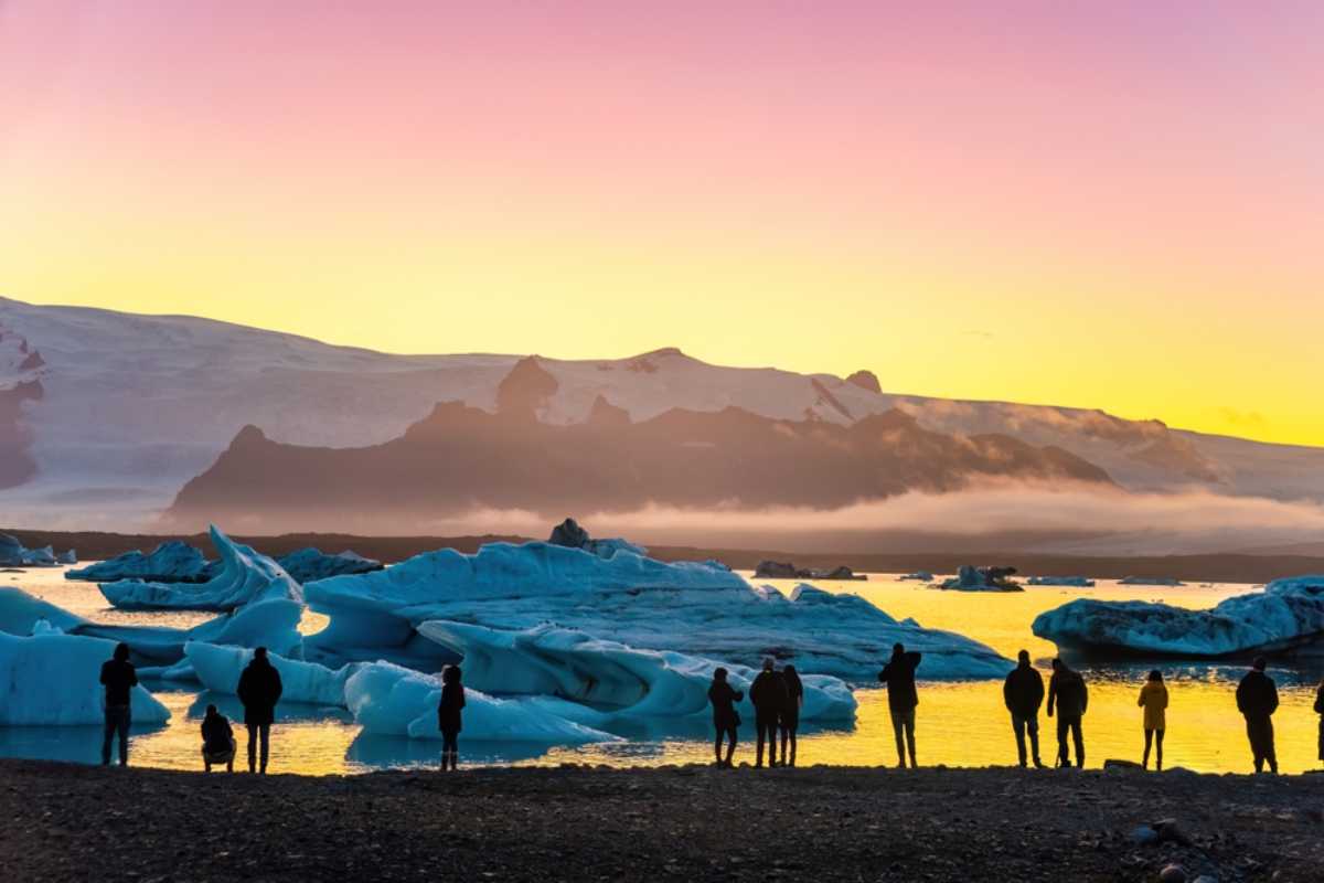 Travelers watching icebergs at Jökulsárlón glacier lagoon during sunset.