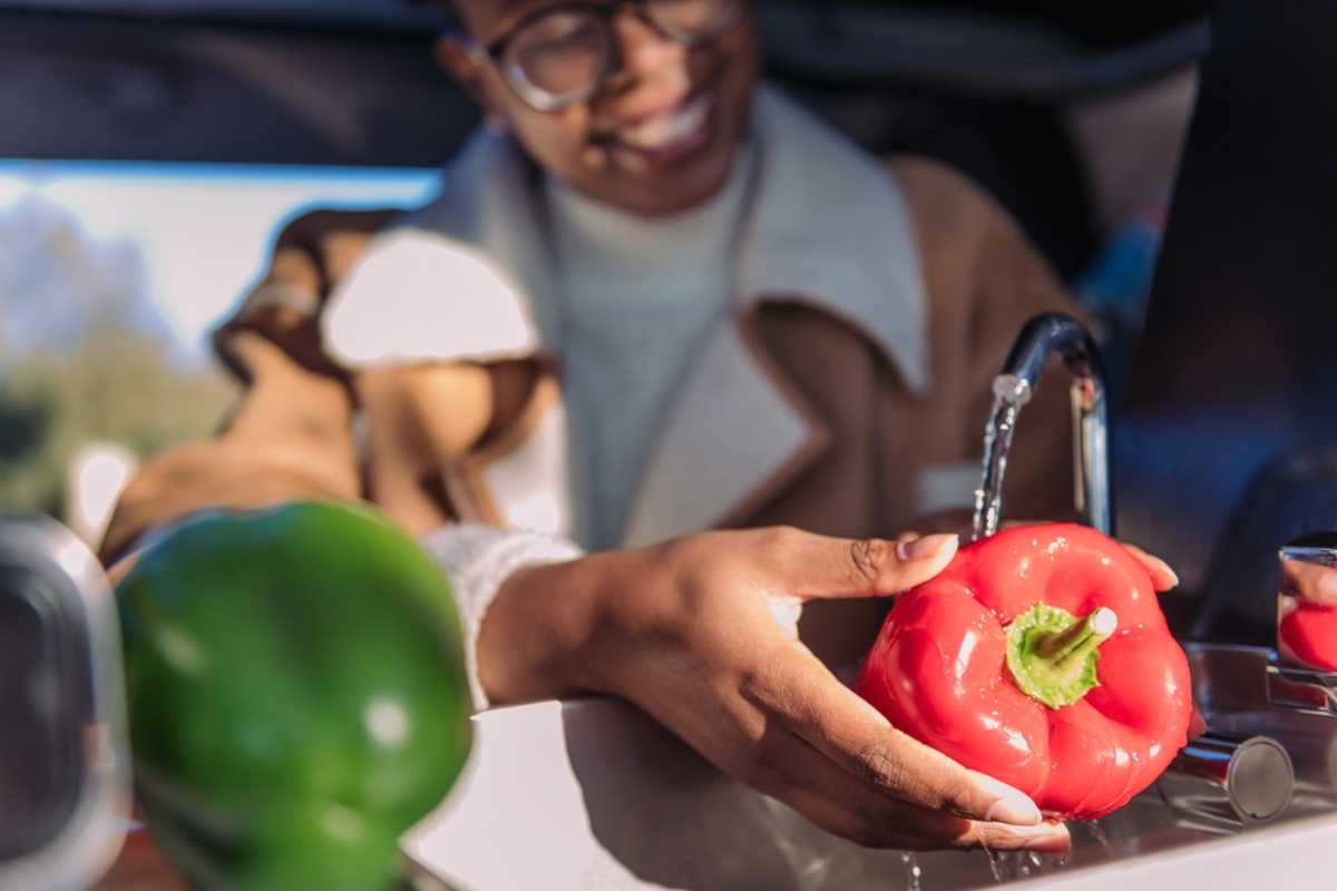 Traveler washing a red bell pepper in a campervan kitchen during an Iceland trip.