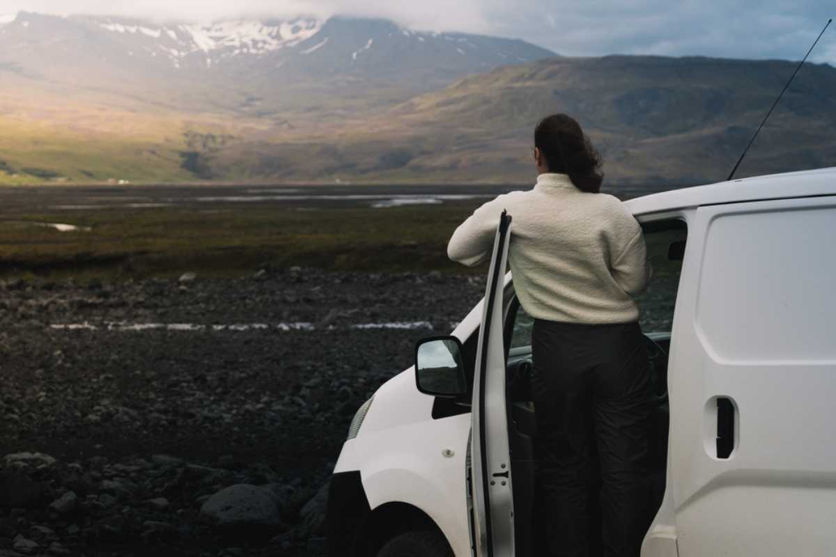 Traveler standing beside a white campervan in a volcanic valley in Iceland.