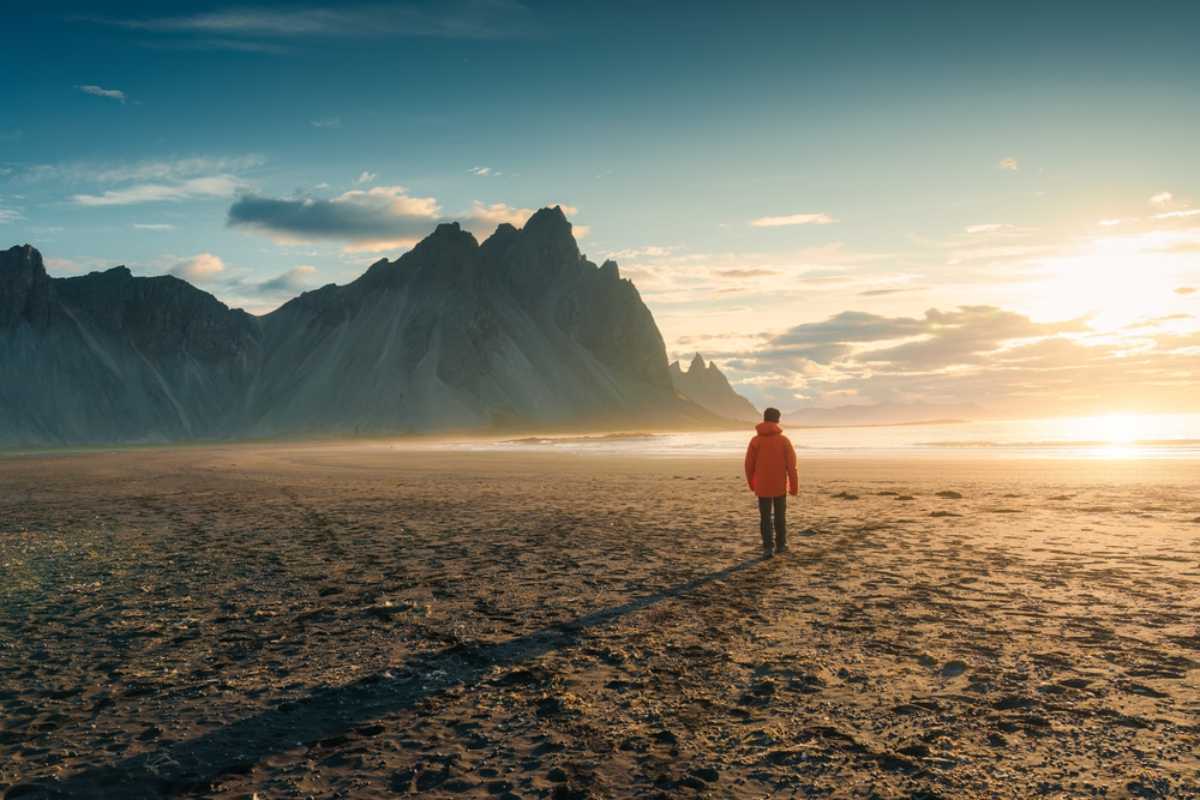 Traveler standing on a black sand beach near Vestrahorn at sunset.