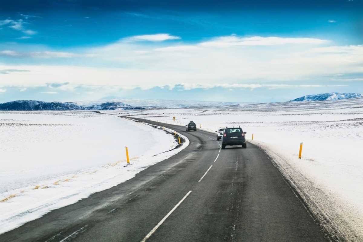 Cars driving along an open Icelandic road surrounded by snow-covered landscapes.