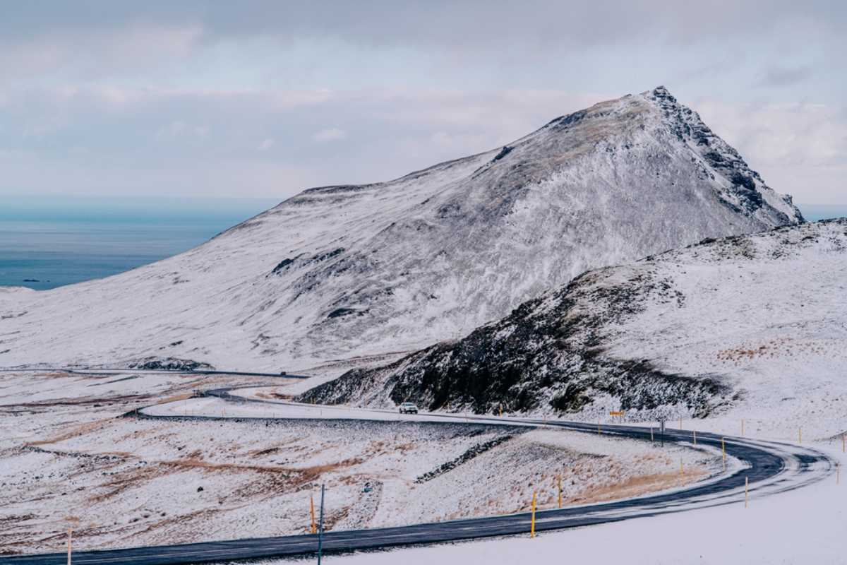 Snowy mountain road in Iceland with a car driving through winter scenery.