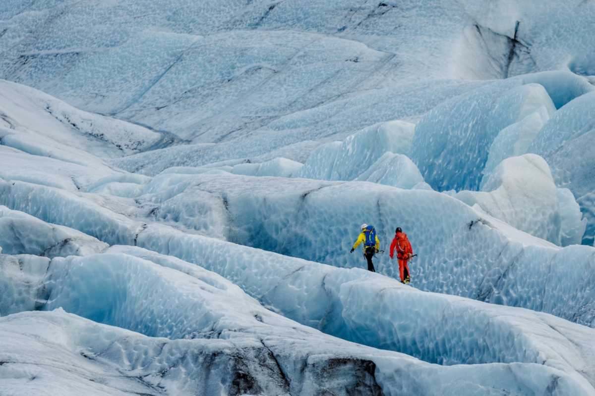 Guided glacier hikers walking across blue ice formations in Iceland.