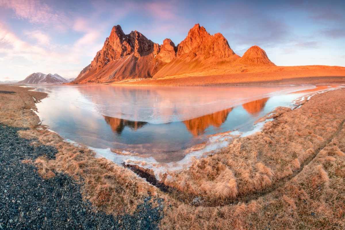 Der Vestrahorn-Berg spiegelt sich bei goldenem Licht im ruhigen Wasser in Island.
