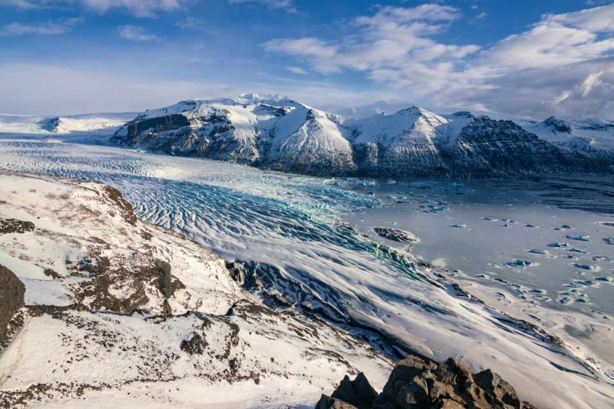 Panoramablick auf einen Gletscher und eine eisige Lagune, umgeben von schneebedeckten Bergen in Island.