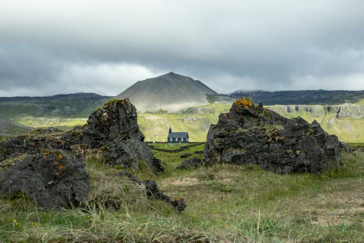 Kleine schwarze Kirche umgeben von Lavagestein und grünen Hügeln auf Snæfellsnes, Island.