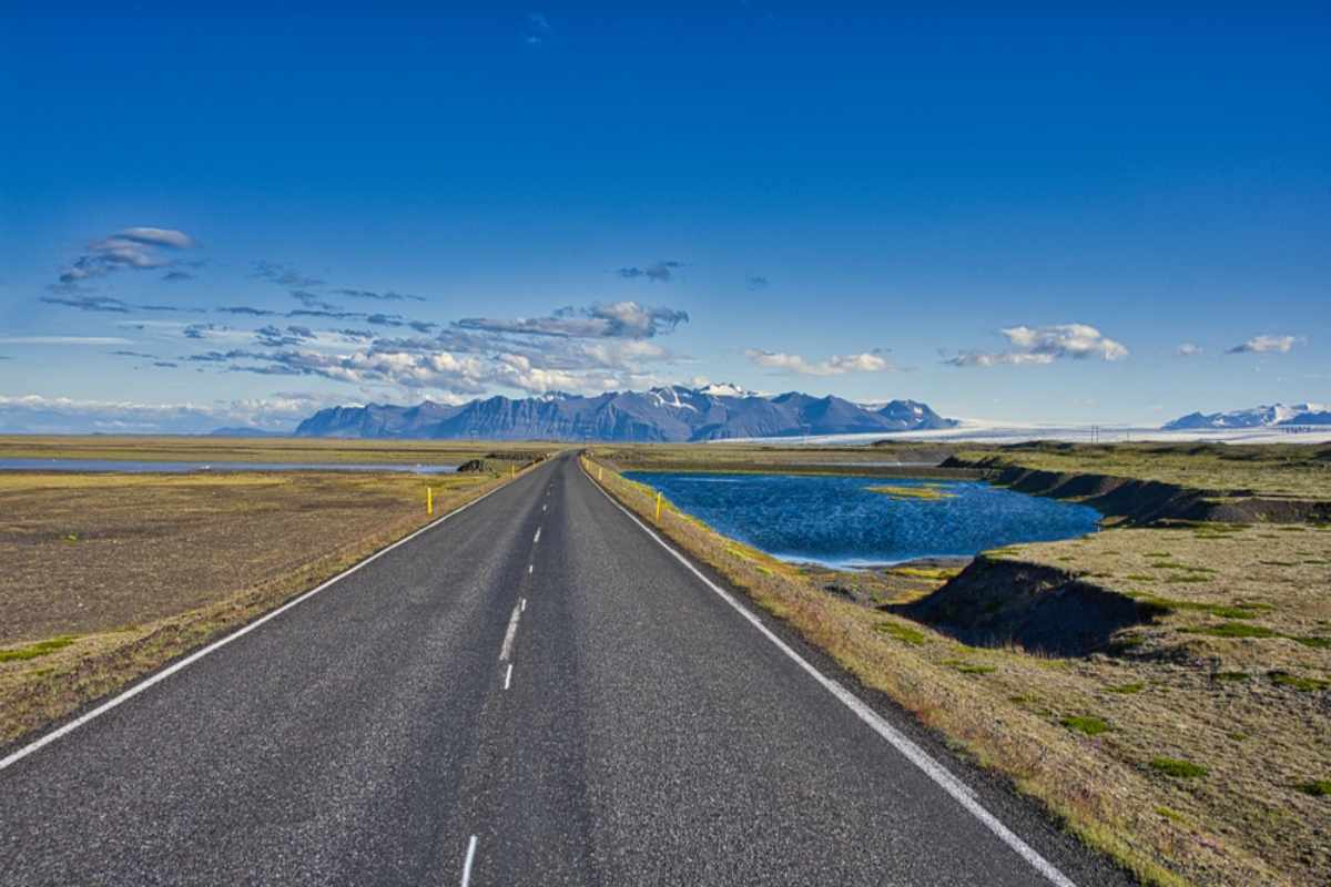 Offene Straße in Island, die sich in Richtung Berge und eines strahlend blauen Himmels erstreckt.