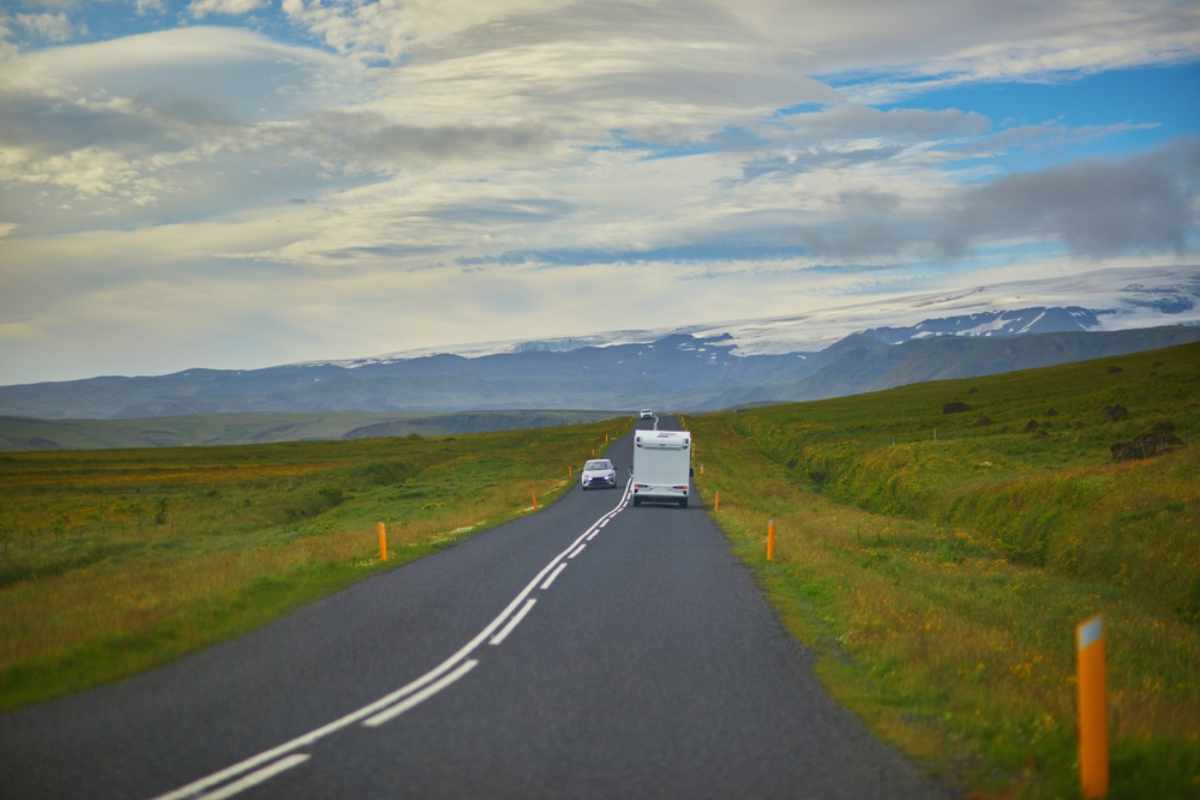 Wohnmobil, das auf einer malerischen isländischen Straße durch grüne Landschaft fährt.