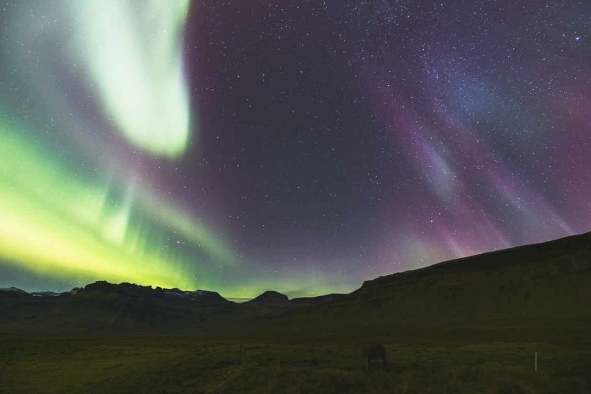 Nordlichter, die über einer dunklen isländischen Landschaft unter einem Sternenhimmel leuchten.
