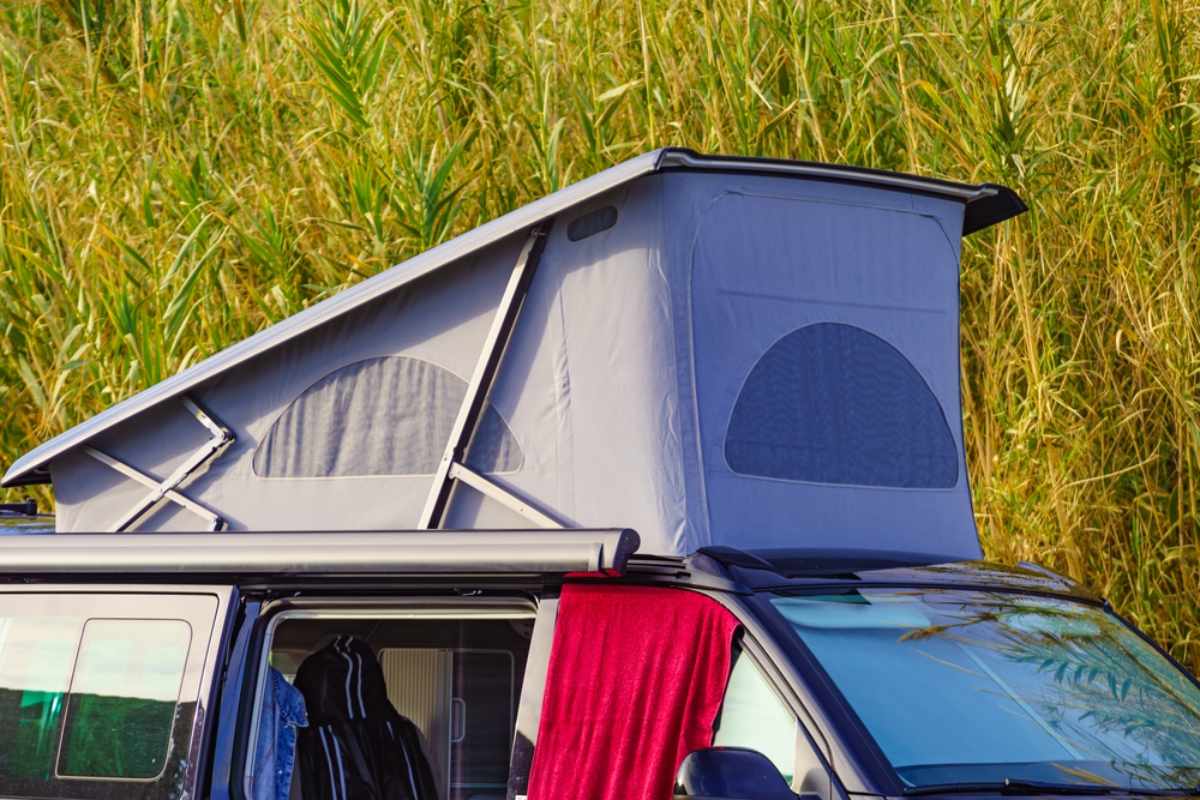 Aufgestelltes Pop-up-Campervan-Dach neben hohem Gras auf einem Campingplatz.