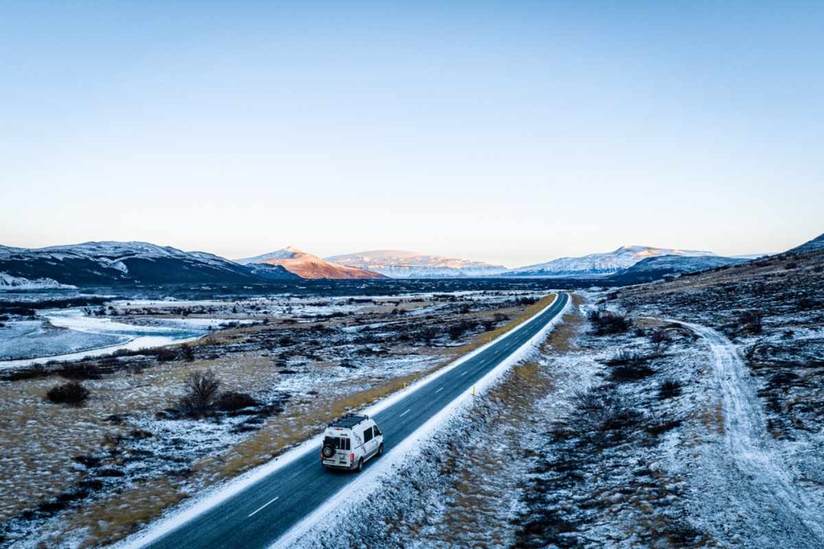Campervan, der eine verschneite Straße durch ein isländisches Tal entlangfährt.