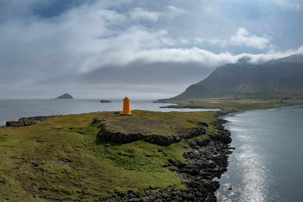 Oranger Leuchtturm an einer abgelegenen grünen Küste in Ostisland.