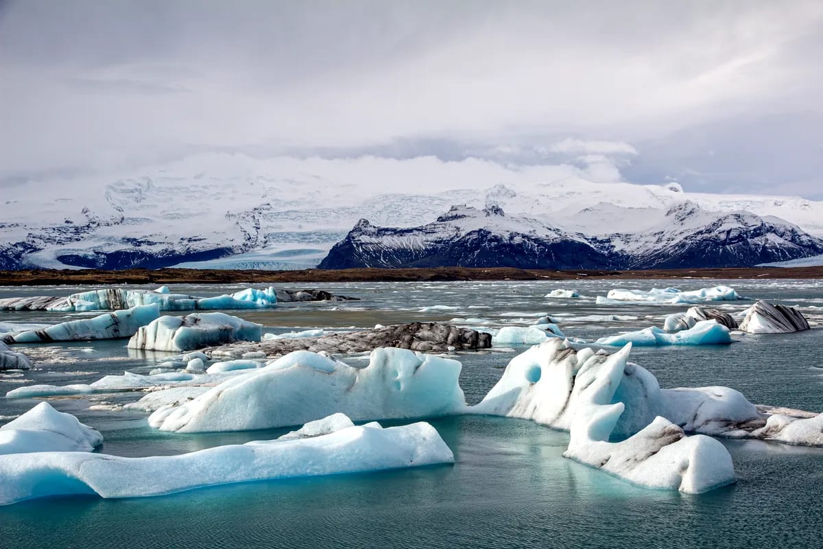 Blue icebergs floating in Jökulsárlón Glacier Lagoon, with snowy mountains, glacial water, and cloudy March skies in South Iceland