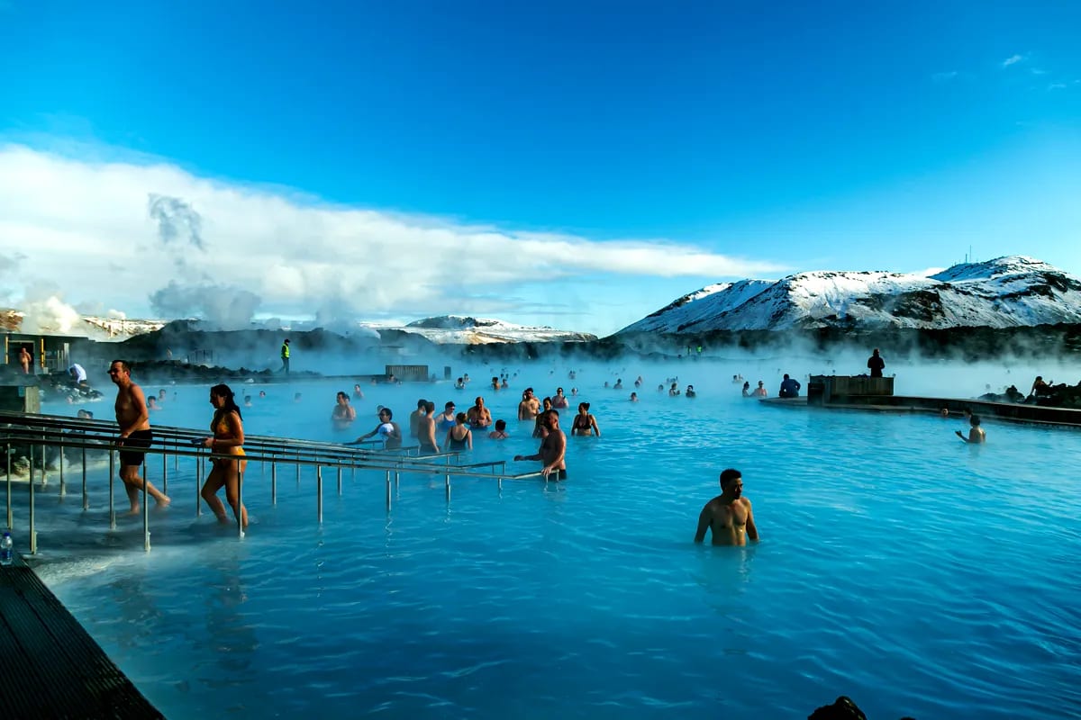 People bathing in Iceland’s Blue Lagoon geothermal spa, with turquoise water, rising steam, and snowy lava fields under bright March skies