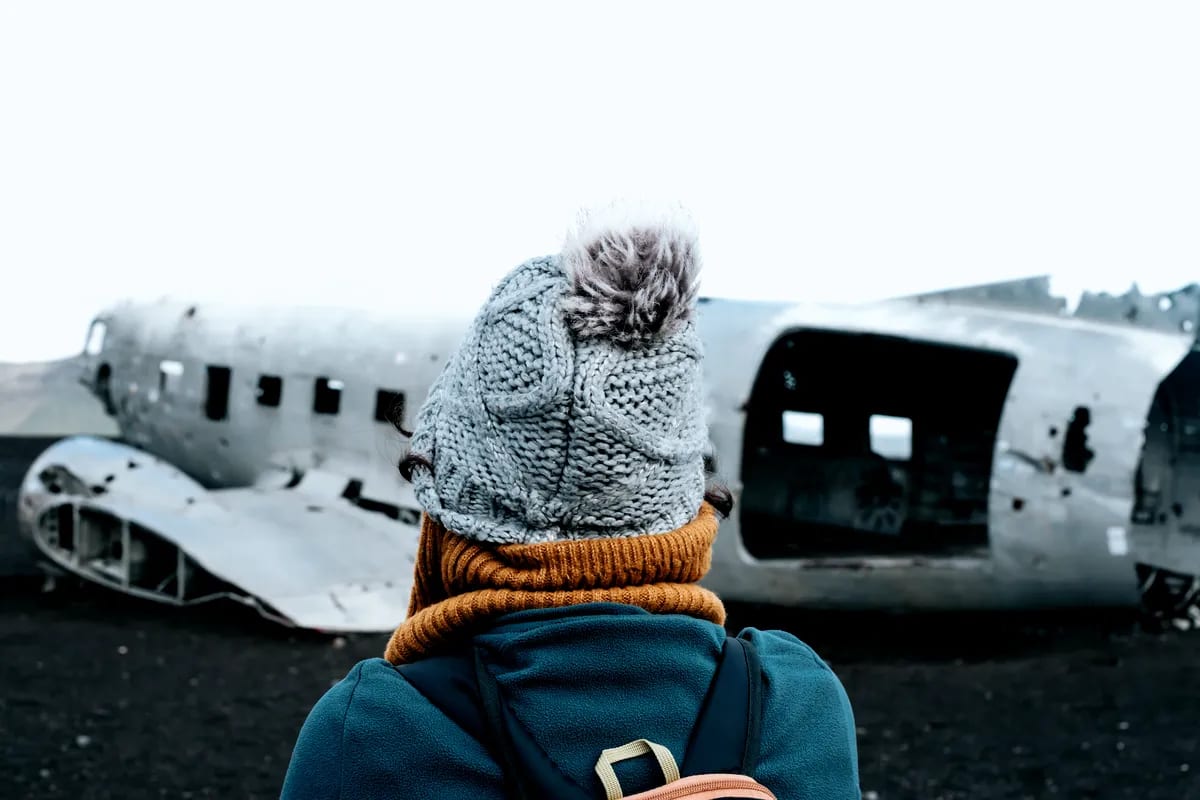Traveler viewing the Sólheimasandur plane wreck on Iceland’s black sand beach, bundled in winter layers beneath misty March skies