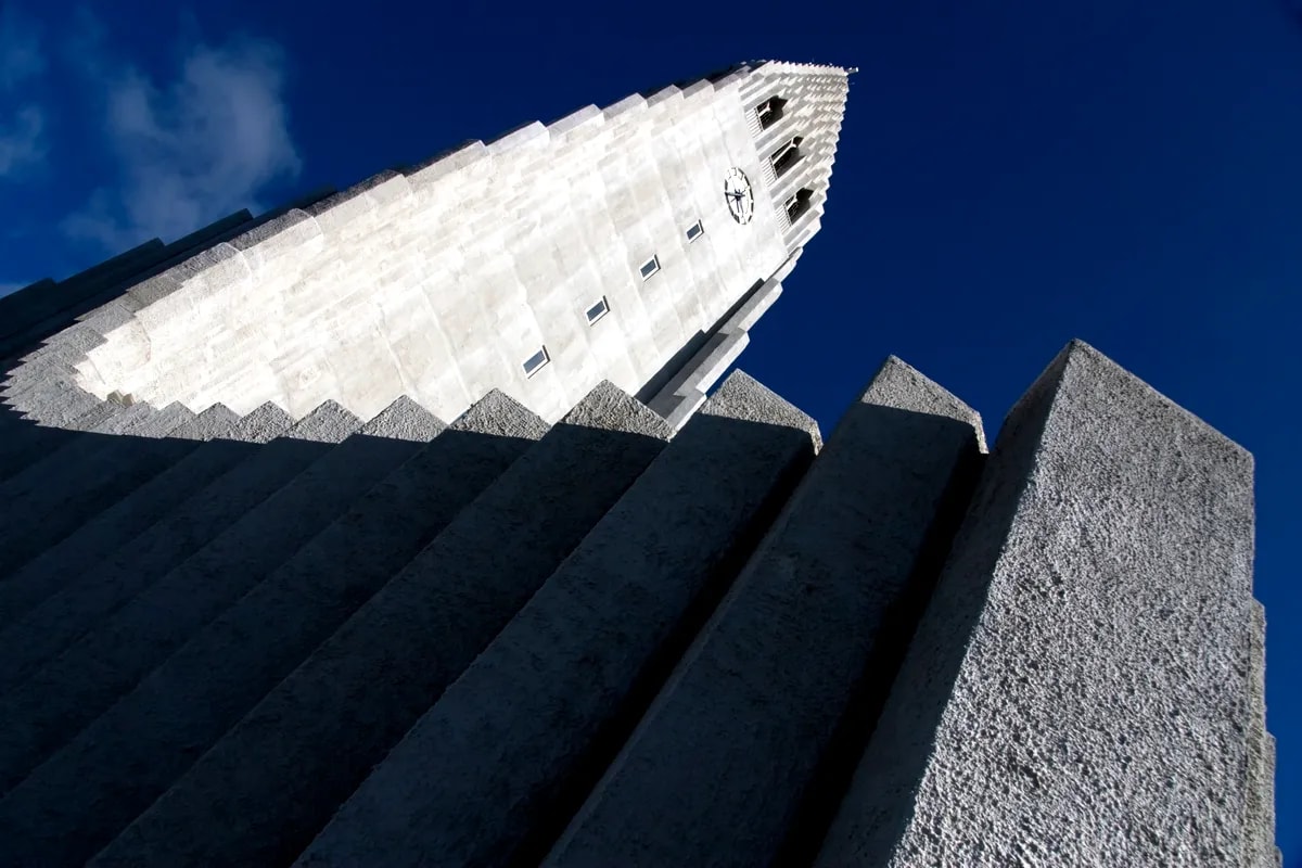 Low-angle view of Hallgrímskirkja church tower and basalt-inspired concrete columns against deep blue sky in Reykjavík, Iceland.