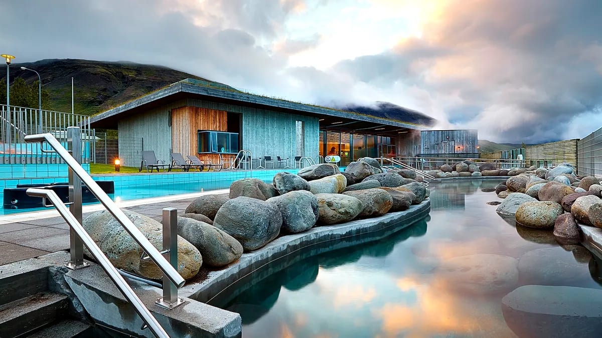 Laugarvatn Fontana geothermal spa with steaming pools, natural rocks, turf-roofed building and dramatic Iceland mountain sunset views