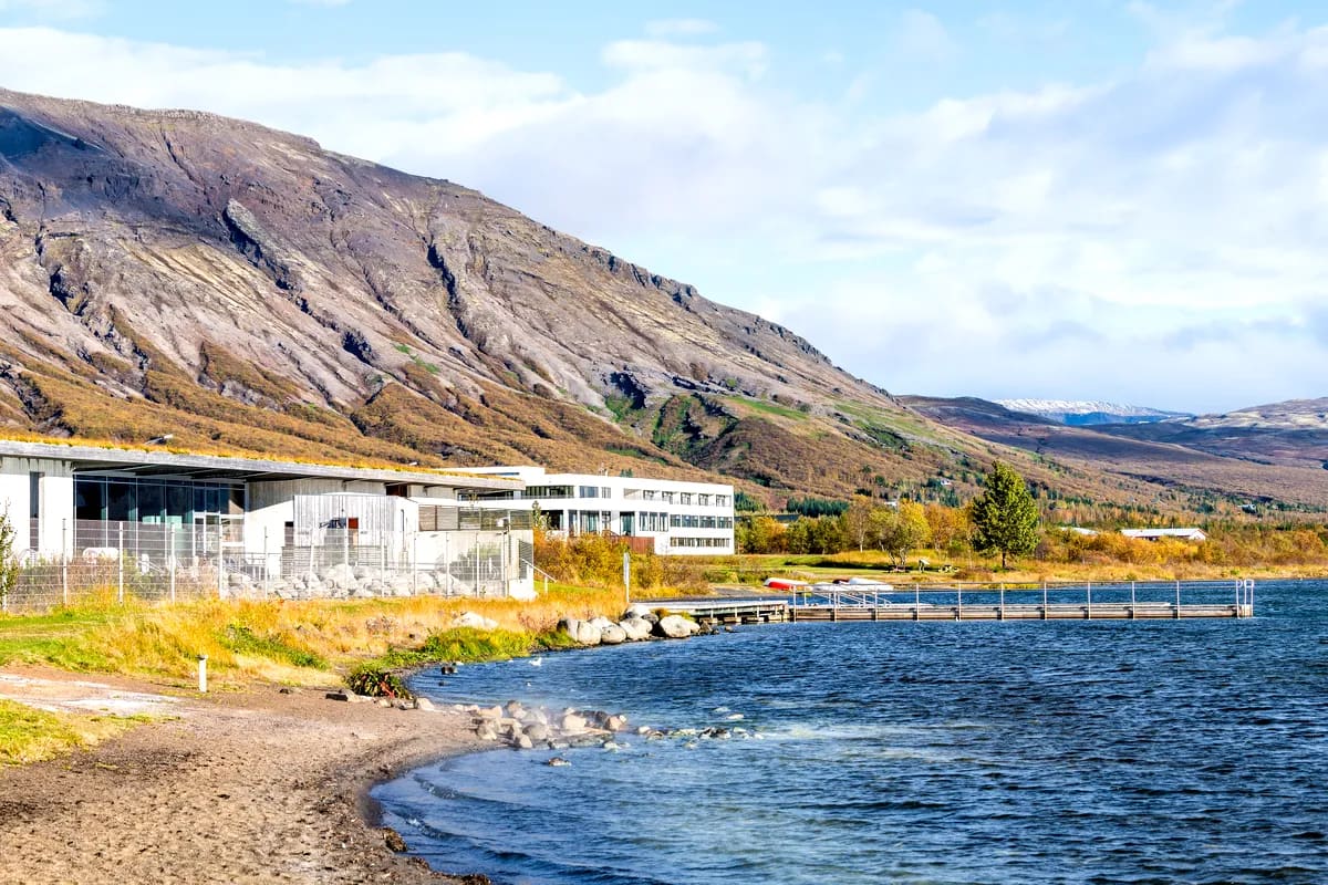 View of Laugarvatn Fontana by Lake Laugarvatn with geothermal steam rising, wooden pier, modern spa building and Icelandic mountains