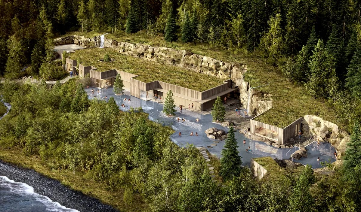Aerial view of Forest Lagoon in Iceland, with geothermal pools, wood buildings, turf roofs, rocky cliffs and dense green forest by the shore.