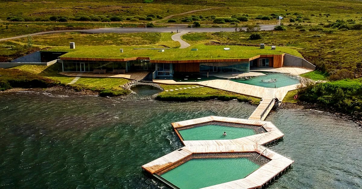 Aerial view of Vok Baths in Iceland with hexagonal floating geothermal pools, wooden walkways, turf-roof spa and green lakeshore