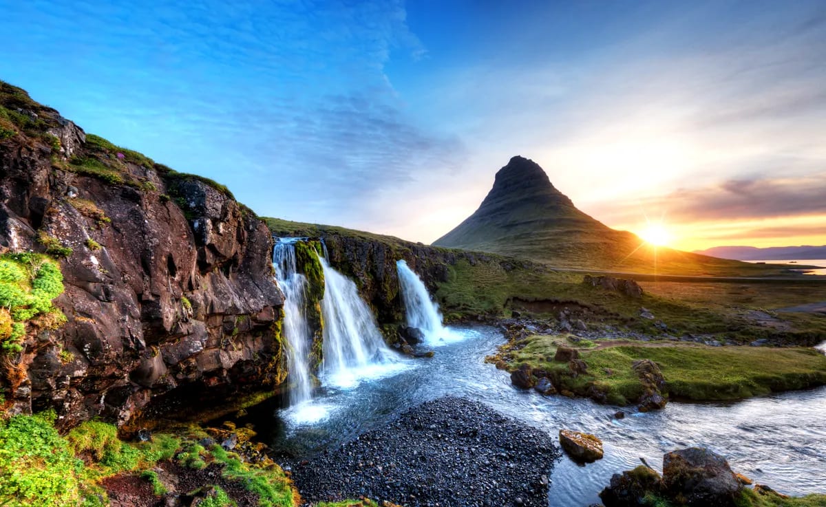 Kirkjufell mountain at sunset with cascading waterfalls, rocky river and green May landscape on Iceland’s Snæfellsnes Peninsula